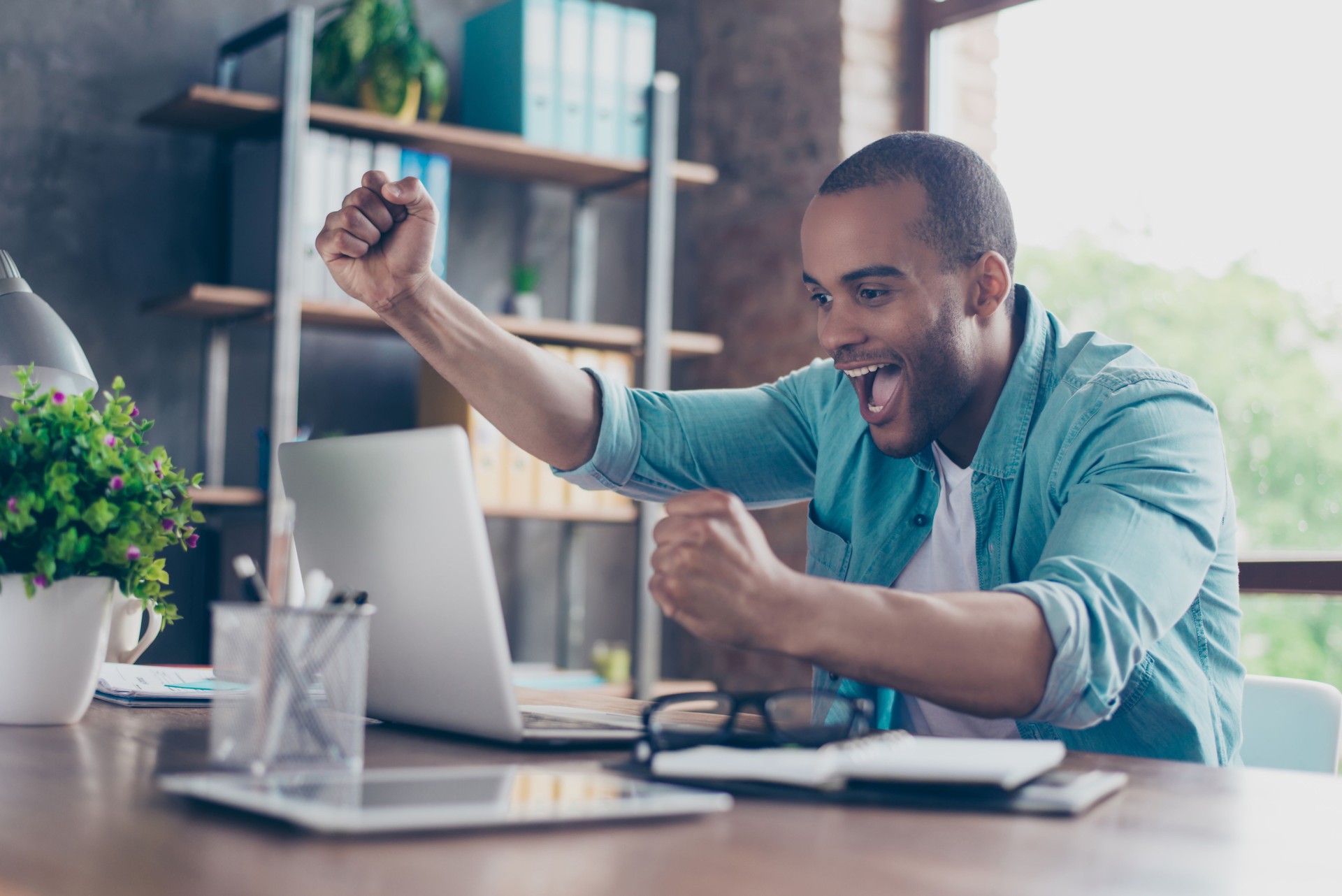 Winner! A dream of the young afro american entrepreneur came true. He is very excited, wearing smart casual, celebrating in the office